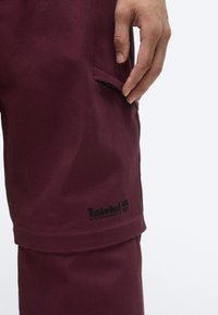 Bordeauxkleurige shorts gemaakt van duurzaam materiaal, met een zijzak met zwarte afwerking en een geborduurd logo aan de zoom.