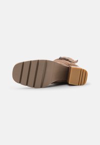 Botte marron avec un dessus texturé, dotée d'une semelle en caoutchouc. La semelle a des rainures horizontales distinctes et un talon bloc pour la stabilité.