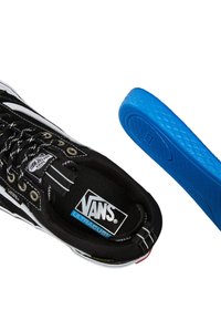 Svarta Vans-skor har en slitstark övre del i canvas med vita detaljer och metallöglor. En klarblå innersula visas separat.