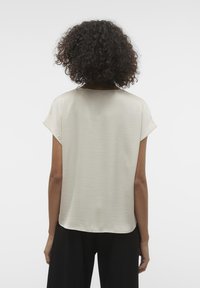 Blouse à manches courtes, beige clair, avec une texture lisse, une coupe décontractée, un col rond et un léger éclat. Vue de dos mettant en valeur la silhouette ample.