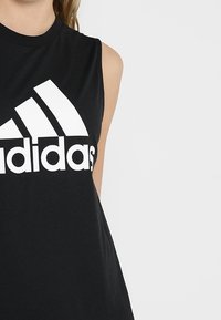 Černý bezrukávový sportovní top s kulatým výstřihem, který má výrazné bílé logo Adidas a design tří bílých diagonálních pruhů.