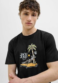 Schwarzes Baumwoll-T-Shirt mit einem Grafikmotiv eines Skeletts, das unter einer Palme entspannt, mit dem Text "JACK & JONES" und "GREAT VIBES."