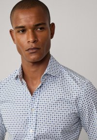 Koszula z guzikami w jasnoniebieskim kolorze z granatowym geomtricznym wzorem na kafelkach, z klasycznym kołnierzykiem, długimi rękawami i dopasowanym krojem.