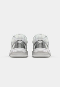 Witte en zilveren sportschoenen met een bovenwerk van mesh, een gewatteerde kraag en een comfortabele zool, met reflecterende accenten en gebogen ontwerp lijnen.