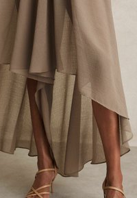 Vestito midi fluido in tessuto beige testurizzato con orlo asimmetrico a strati. Abbinato a tacchi a strisce marrone chiaro.