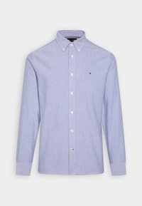 Světle modrá košile s dlouhým rukávem, zapínáním na knoflíky a kravatou s knoflíky, s malým vyšitým logem na levé části hrudi.