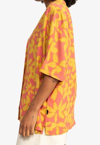 Short-sleeve shirt in pink with a large yellow floral pattern. Made from a lightweight fabric, featuring a relaxed fit and side slits.