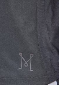 Mörkgrå atletisk t-shirt med en texturerad tyg, som har en subtil logotyp i en ljusare nyans på den nedre vänstra sidan och kontrasterande söm-detaljer.