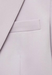 Revers de blazer violet clair et poche poitrine avec une texture de tissu finement tissé, montrant des détails de coupe nette et de coutures soignées.