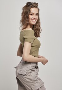 Top ajustado color verde oliva con textura acanalada, combinado con pantalones cargo grises claros que tienen bolsillos laterales y un corte relajado.