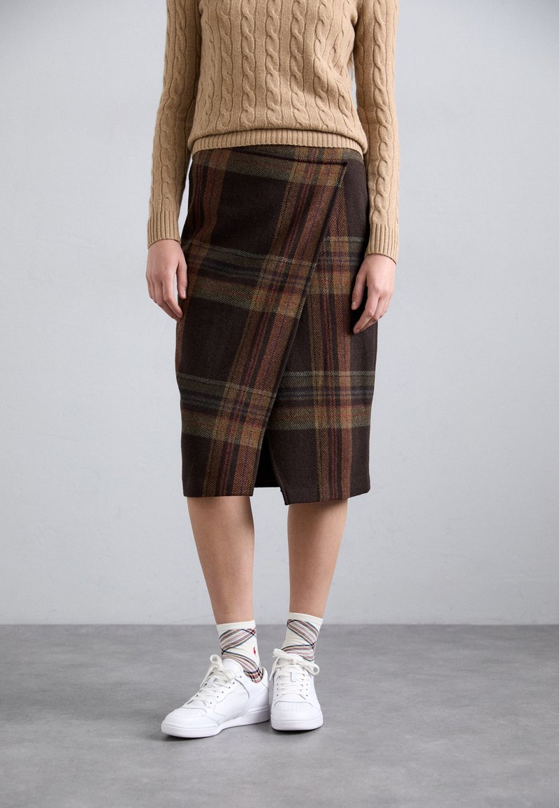 Brown plaid wrap skirt made of wool, featuring green, orange, and yellow stripes. Paired with white sneakers and patterned socks.