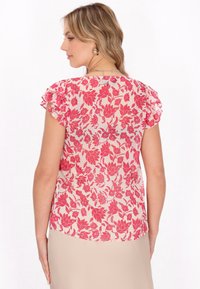 Blomstret bluse i let stof med røde og lyserøde blomstermønstre, korte flæseærmer og en rund bagkant. Blød tekstur, gennemsigtig look.