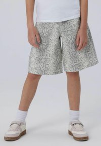 Shorts a stampa snake grigia e bianca, di lunghezza fino alla coscia, realizzati in tessuto leggero. Abbinati a calzini bianchi testurizzati e sneakers.