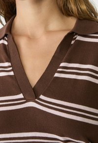 Brązowy i biały polo w paski wykonane z dzianiny, z dekoltem w kształcie litery V, z ribbowanym kołnierzykiem i teksturowanym materiałem. Skupienie na dekolcie i wzorze w paski.