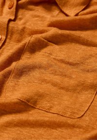 Roodbruine, button-up blouse van gestructureerde stof. Beschikt over een borstzak en knopen in natuurlijke tinten. Zachte, casual uitstraling.