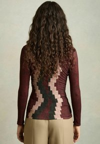 Maglietta a maniche lunghe con un design a motivo di zigzag in color bordeaux, rosa e nero. Il tessuto appare testurizzato con una silhouette aderente.