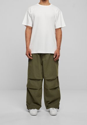 Hvid t-shirt med korte ærmer, parret med løse olivengrønne cargo-bukser, der har flere forlommer og opsmøgede bukseben. Hvide sneakers.
