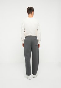 Pantalones de chándal grises con un ajuste relajado y cintura elástica, que cuentan con un bolsillo trasero. Llevados con una camiseta de manga larga de color claro.