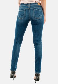 Jeans skinny en denim bleu moyen, avec des poches arrière dotées de coutures en zigzag et d'une étiquette en cuir au niveau de la ceinture. Texture lisse, ajustement sur mesure.