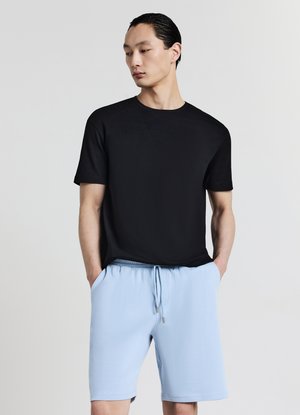 Maglietta nera in cotone con maniche corte abbinata a pantaloncini azzurri chiari con coulisse. Design semplice, vestibilità comoda, tessuto liscio.