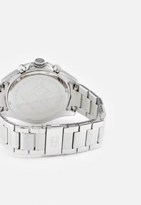 Montre en acier inoxydable avec un bracelet et un boîtier métalliques polis. Équipée d'une couronne texturée et d'un logo de marque gravé au dos.