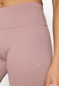 Light pink high-waisted leggings with a smooth texture, featuring discreet logo detail and subtle stitching along the waistband.