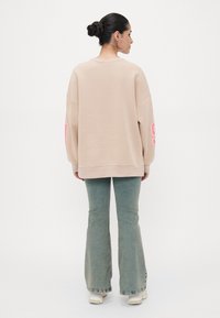Felpa beige oversize con grafica rosa sulla manica, abbinata a jeans flare azzurri. Tessuto morbido e design comodo.