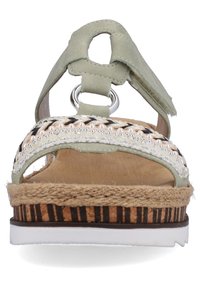 Sandale en cuir vert avec semelle en caoutchouc, accents tissés beiges et noirs, et détails en jute tressé. Le design ouvert au niveau des orteils présente un anneau en métal circulaire.