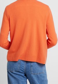 Orangemönstrad stickad tröja med avslappnad passform, ribbad nederkant och enkel design. Bärs med högmidjade blå denim jeans.