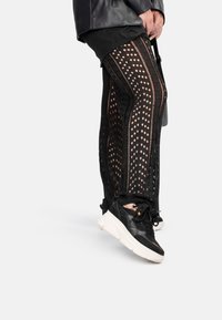 Schwarze Mesh-Leggings mit Ausschnitten und seitlichen Nähten, kombiniert mit schwarz-weißen Sneakern. Sie verfügen über einen strukturierten Stoff und eine figurbetonte Passform.