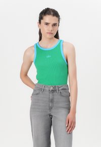Top verde cu dungi, cu margine albastru deschis, având în centru logo-ul 'GAP', asortat cu blugi gri cu talie înaltă. Textură netedă.