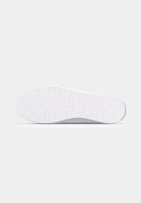 Semelle d'une basket blanche avec motif répétitif du texte « Tommy » et formes de cœurs embossées à la surface.