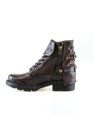 Bottine en cuir marron foncé avec fermeture éclair latérale, rabat décoratif et clous métalliques autour du talon sur fond blanc.