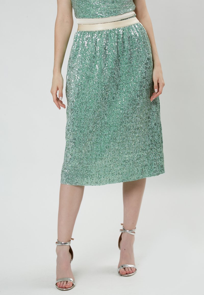 Falda verde esmeralda con lentejuelas, de longitud a media pantorrilla, diseño plisado y cinturilla color crema. Se lleva con sandalias plateadas de tiras.