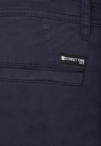 Pantalones azul marino de tela suave, con un bolsillo trasero y una etiqueta negra con el texto "STREET ONE". Detalle de costura bien cuidada visible.