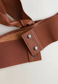 Brun bälte med en texturerad lädersektion, kontrasterande slät tyg och metallknappar för stängning. Snurrad tygdetalj ingår.