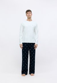 T-shirt en coton blanc à manches longues avec détail de boutons, associé à un pantalon de pyjama bleu marine à motifs avec de petits motifs multicolores.