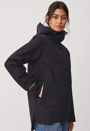 Giacca nera impermeabile con cappuccio, tasche anteriori e cordini regolabili. Tessuto morbido, orlo posteriore leggermente allungato, logo sulla manica.