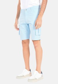 Pantaloni cargo azzurro chiaro in cotone, caratterizzati da tasche laterali, chiusura con bottone e una vestibilità comoda. Indossati con sneakers bianche e grigie.