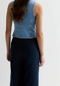 Bezruký deninový crop top v světle modré barvě, s přiléhavým střihem a prošitými švy, spárovaný s tmavými, širokými kalhotami.