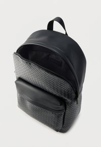 Sac à dos noir avec une texture tissée sur la poche avant et une section supérieure lisse ; fermeture éclair et poignée supérieure pour le transport.