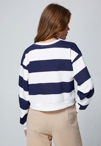 Sudadera corta de rayas en azul marino y blanco, con escote redondo, mangas largas y dobladillo acanalado. Textura suave, diseño casual, sin logotipos visibles.