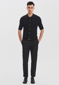 Czarna koszula z krótkim rękawem zapinana na guziki, o fakturowanym wykończeniu, w połączeniu z czarnymi spodniami i butami, tworząc monochromatyczny wygląd.