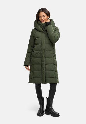 Groene pufferjas met een grote capuchon, doorgestikt ontwerp en zijzakken. Gecombineerd met zwarte jeans en kniehoge zwarte laarzen.
