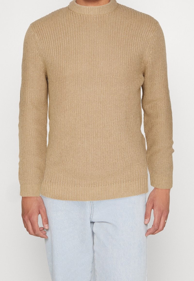 Jersey de punto beige con textura acanalada, cuello redondo y mangas largas. El dobladillo y los puños tienen un diseño acanalado que complementa el conjunto.