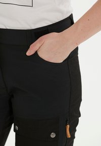 Svarta cargo-byxor i ett stretchigt material, med en sidoplånbok med dragkedja och en klaffficka med metallknappar.