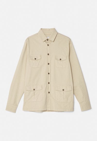 Beige cotton shirt with a collared neck, front button closure, and two chest pockets. Features long sleeves and a relaxed fit.