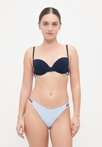 Mørkeblå bikini-top med ribbet tekstur og tynne stropper, kombinert med lyseblå bikinitruser med røde og hvite stripete detaljer.