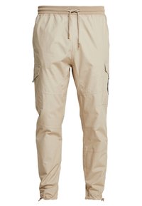 Beige Cargo-Hosen aus weichem Stoff, mit elastischem Bund und Kordelzug, Seitentaschen und zulaufenden Bündchen.