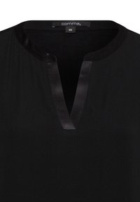 Schwarze Bluse mit V-Ausschnitt, mit satinschimmerndem Besatz entlang des Ausschnitts. Der Stoff wirkt glatt und leicht. Größenetikett sichtbar.
